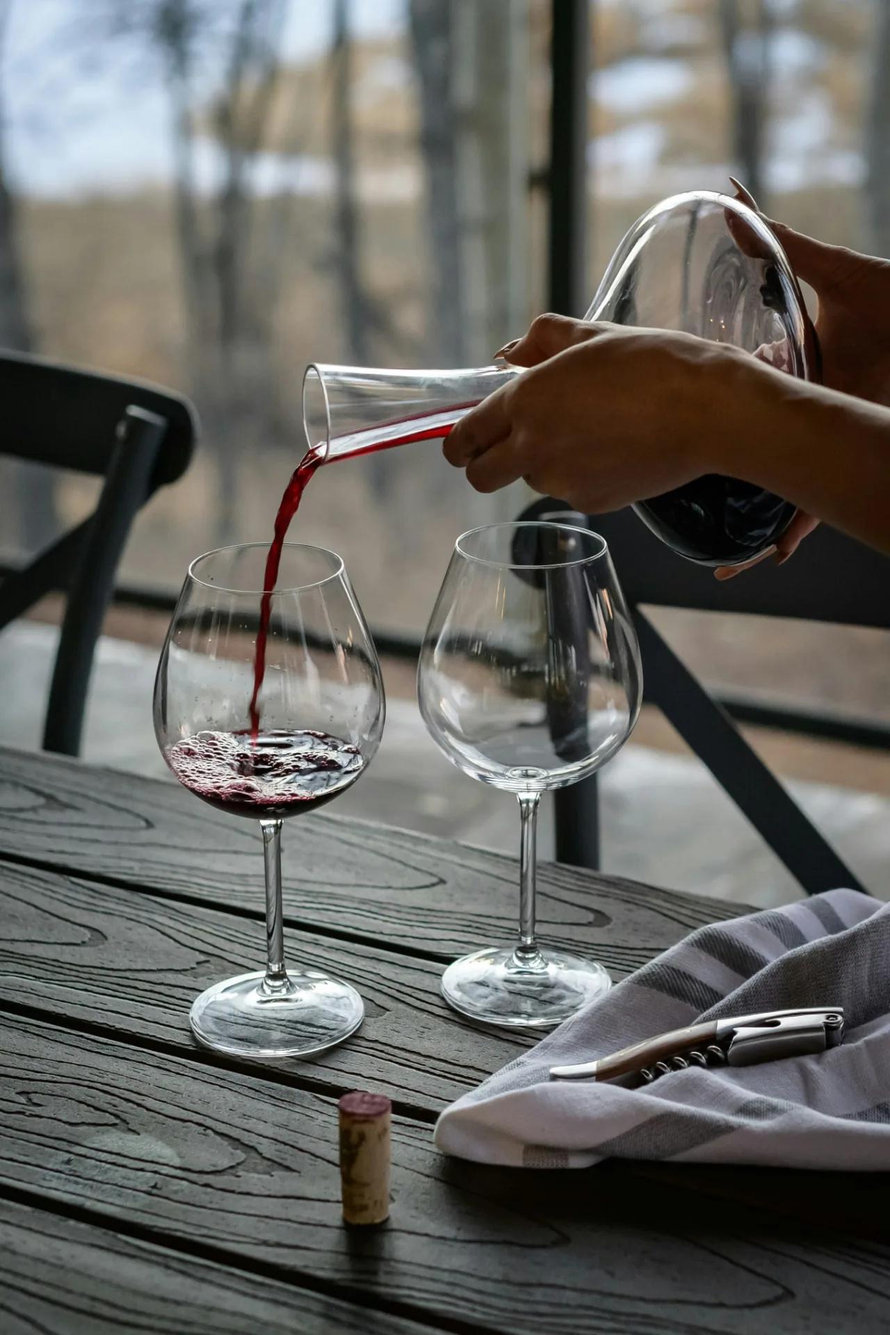 Rode wijn wordt uit een karaf in een glas geschonken op een houten tafel